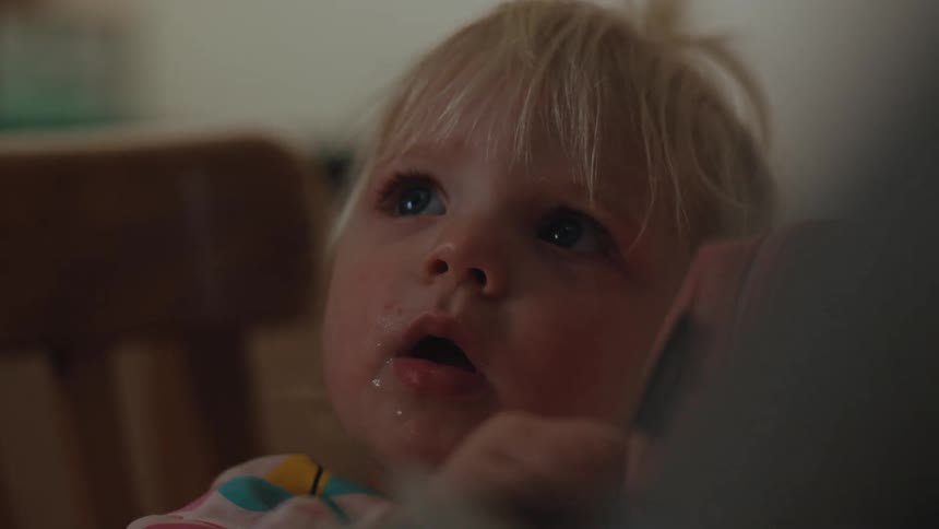 A toddler with a messy mouth stares at another person sitting at the table