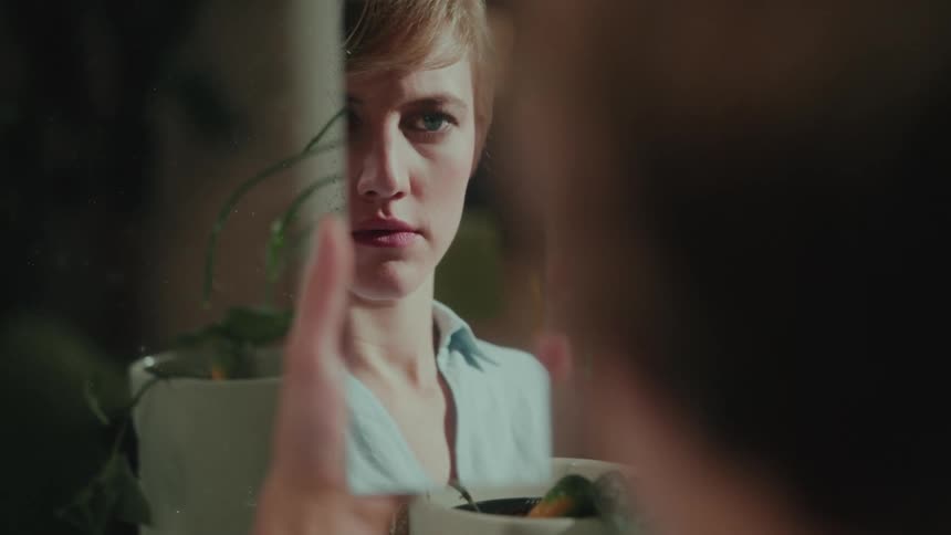 Blonde woman looking at herself in a thin mirror
