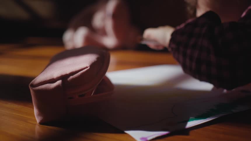 A girl takes out a pen from a pencil case and starts drawing on paper at a table