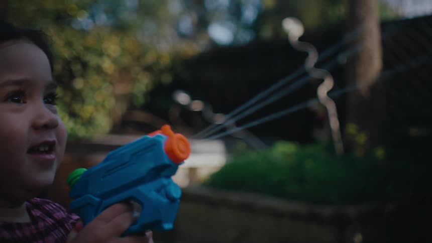 A little girl is running then stops and starts shooting her toy water gun forward