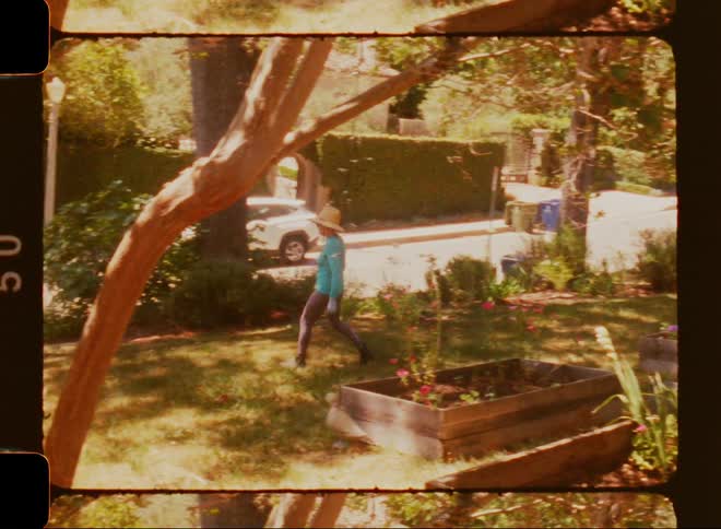 A person is walking in a yard and wearing a hat and blue shirt