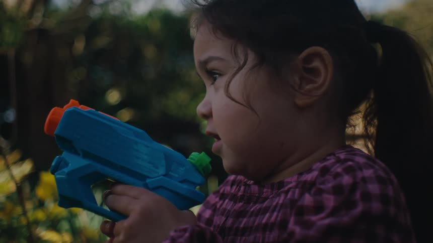 Little girl in a backyard playing with a water spray gun