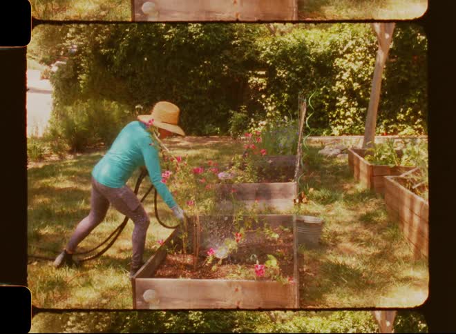 Woman waters plants in a garden bed framed by a border