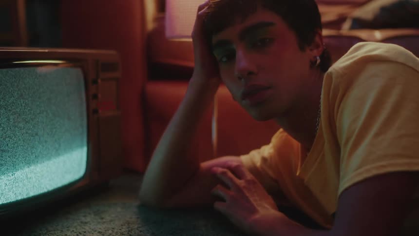Portrait of a young person lying on the bedroom carpet next to a television with no signal