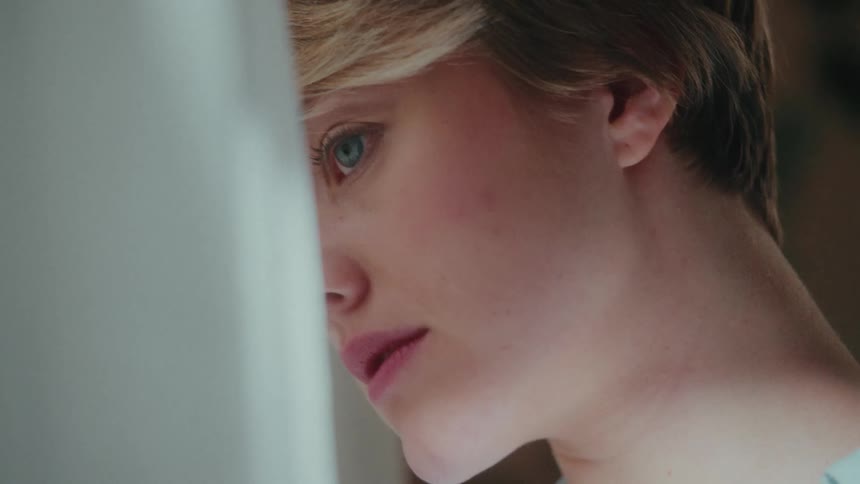 Side portrait of a young blonde woman looking in curtain