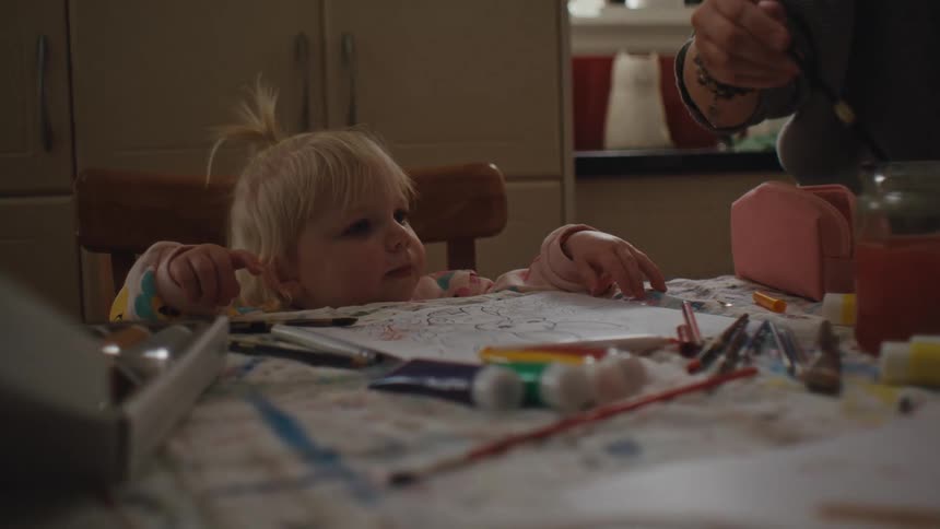 Hand of an adult person handing a paintbrush to a child who is sitting at the table