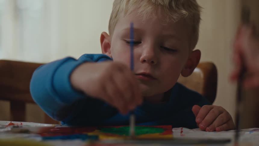 Little boy sitting holding a paintbrush and painting