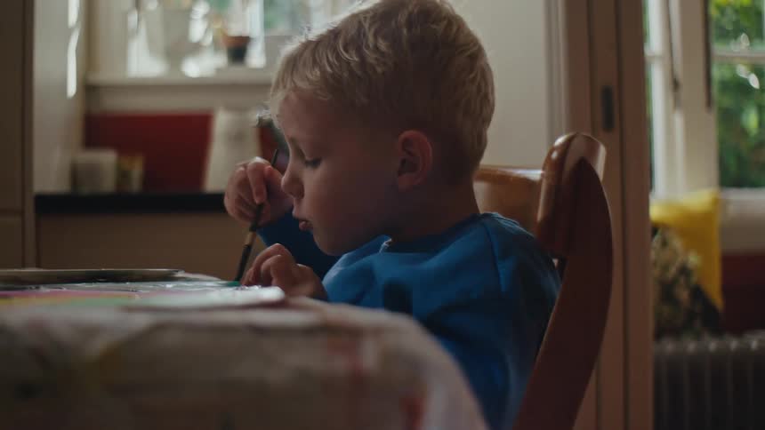 A young boy paints a picture while sitting at a table