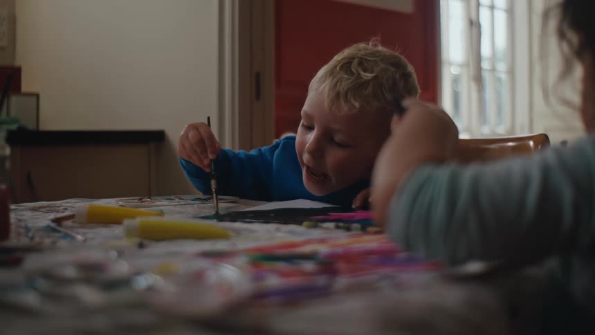 Young children paint while sitting at a table at home during the day