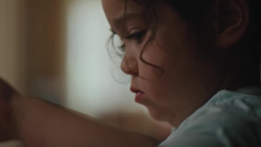 The face of a young girl holding a paintbrush who is painting a white paper
