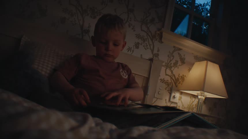 Blonde boy flips through an activity book while sitting in bed in the evening