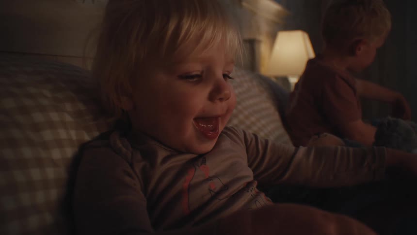 Two children sitting on the bed with one of them reading a book