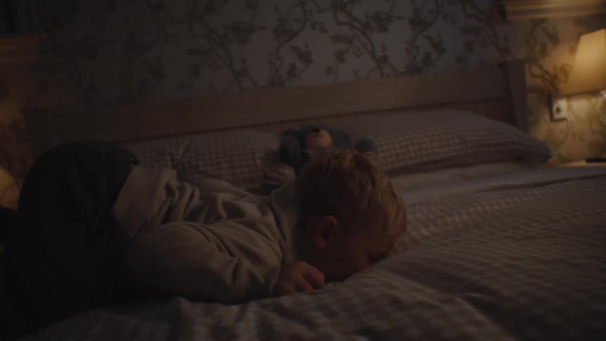 Little blond boy playing on the bed in the bedroom