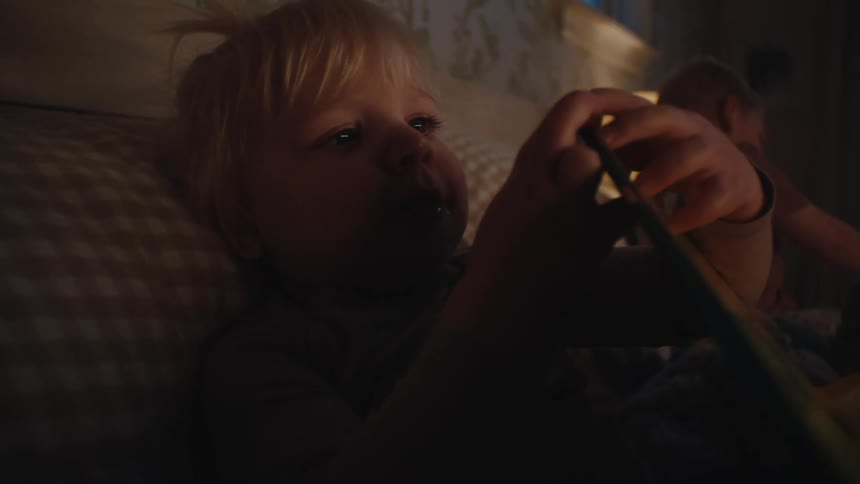 Two small children lying in bed with one of them opening a book