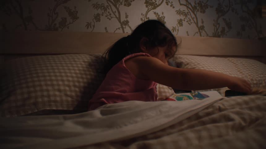 Little girl lying in bed at night playing