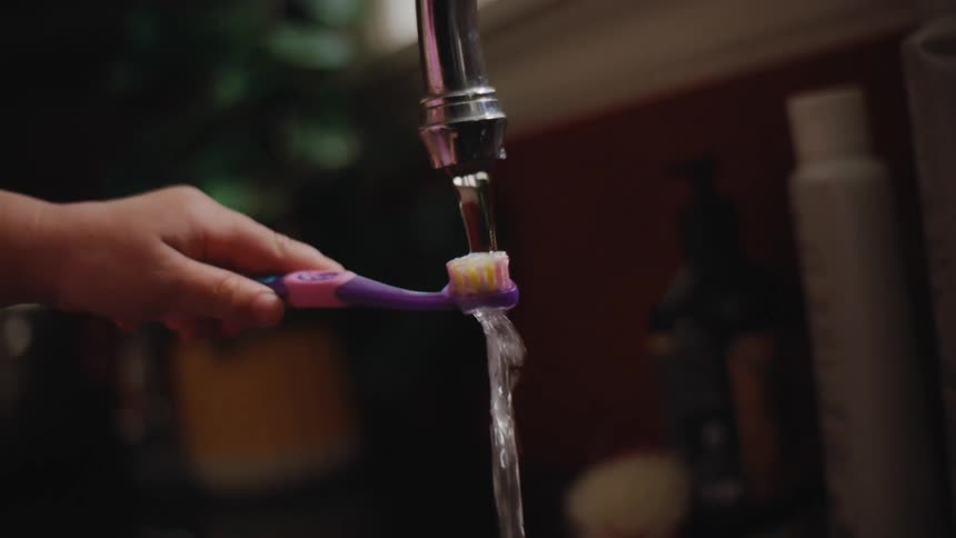 A child wets their toothbrush in the sink