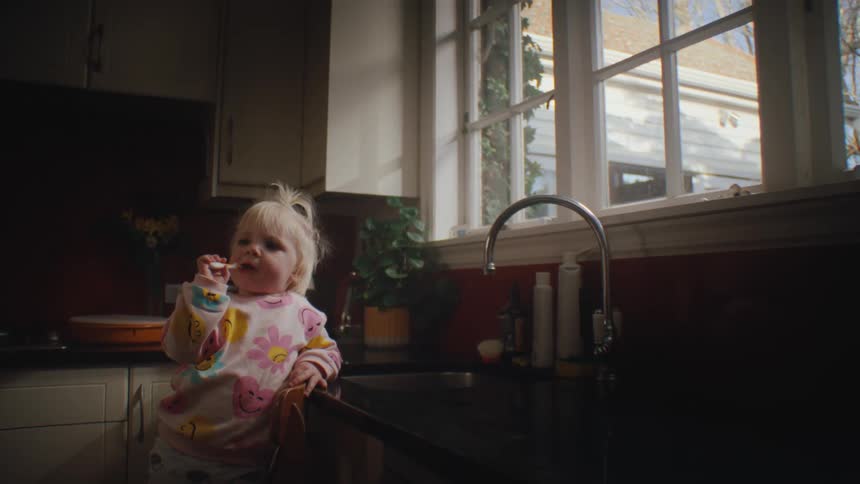Little blonde girl on a chair brushing her teeth