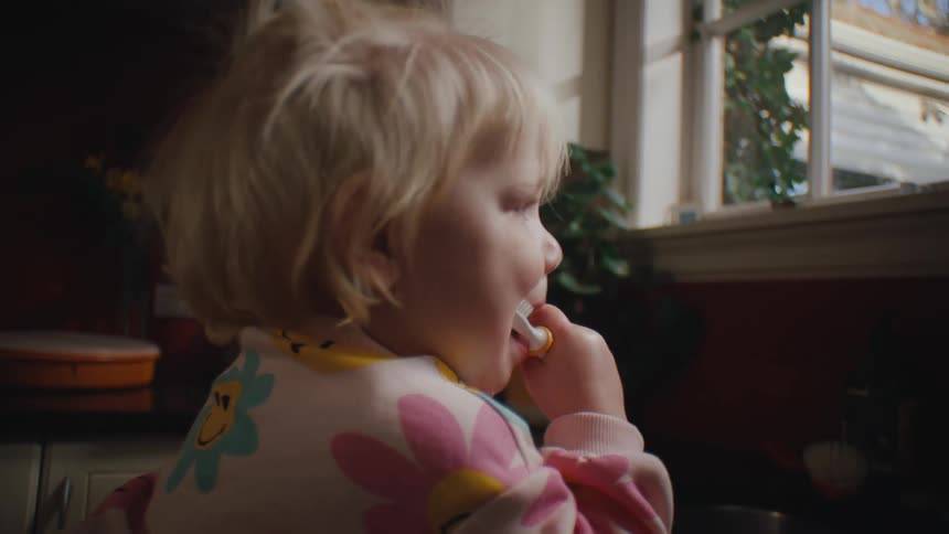 A toddler brushing her teeth at the kitchen sink at home