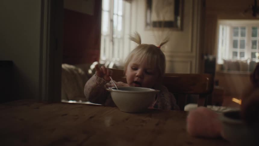 Little girl sitting at table holding spoon inside white bowl