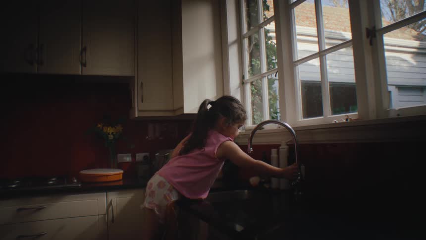 Girl on a chair at the kitchen sink turning off the tap