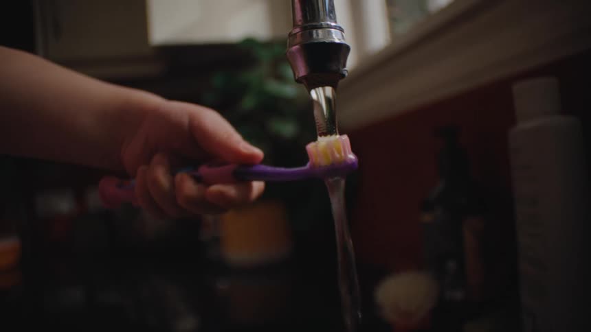 Childs hand as a toothbrush with toothpaste placed in running water in the sink
