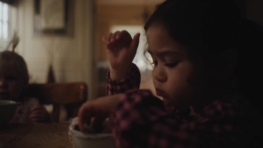 A young girl eats berries out of a bowl on a dining room table