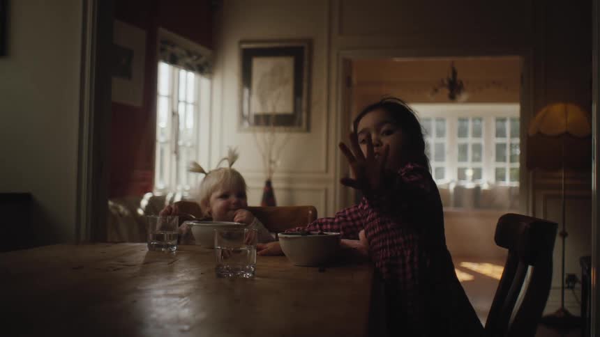 Two young girls sit at a dining room table with food and drink and play around