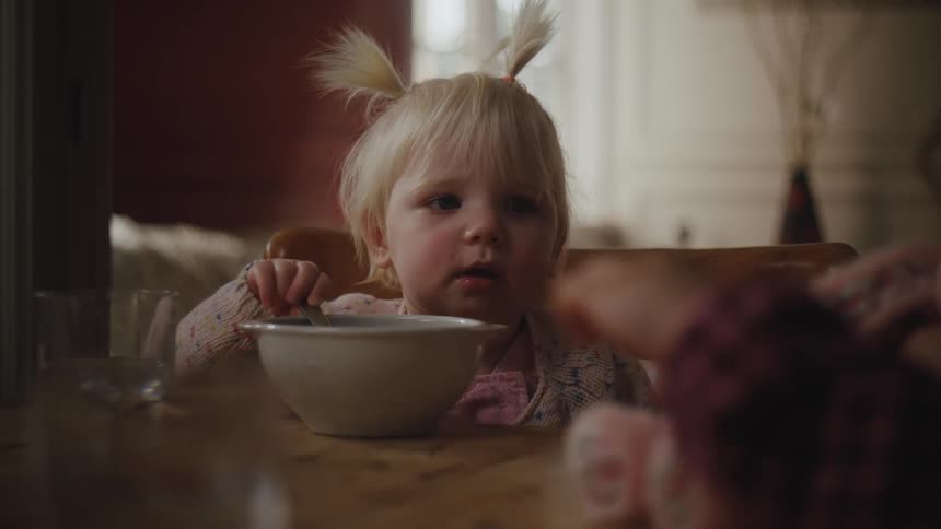 Little blonde girl holding a spoon looking at another child next to her