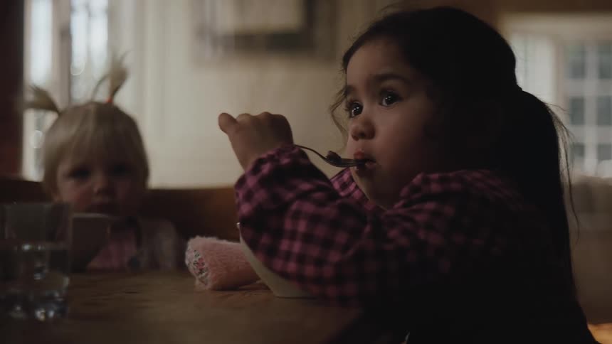 Two children sitting at a table eating cereal from a bowl