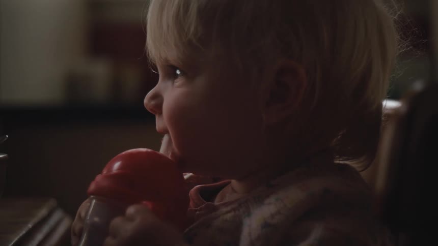 Little blonde girl sitting down drinking liquid from a small bottle
