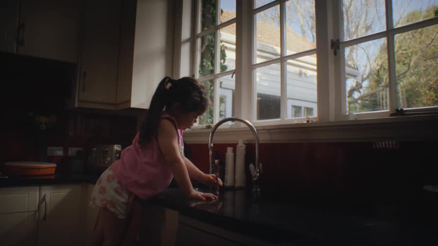 Girl leaning on a chair and turning on the kitchen sink faucet and brushing her teeth