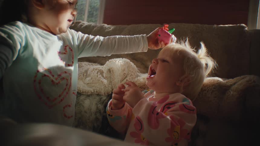 Two small children with toys in their hands playing in the living room