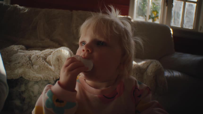 Closeup of a child biting a toy while sitting indoors near a couch