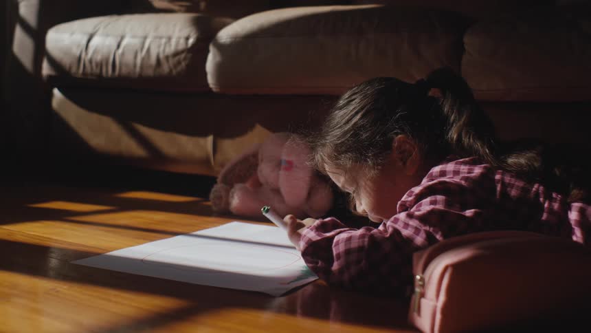 Little girl lying down drawing on a white sheet