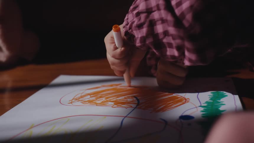 Little girl doodling and drawing with an orange pen on a paper