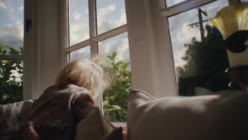 Little blonde girl on the couch in a house next to windows