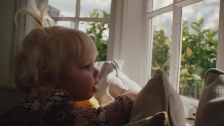 Little blonde girl climbing on the cushions of a sofa indoors