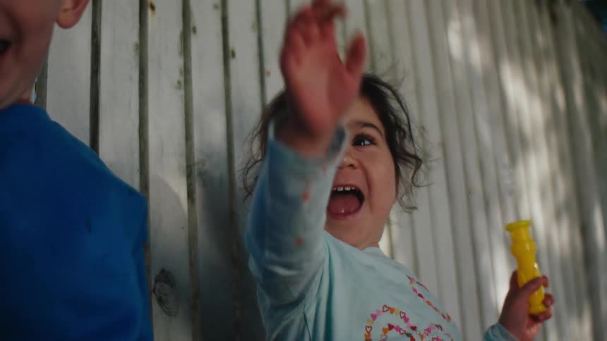 A couple of children recline on a white fence in the backyard playing with soap bubbles