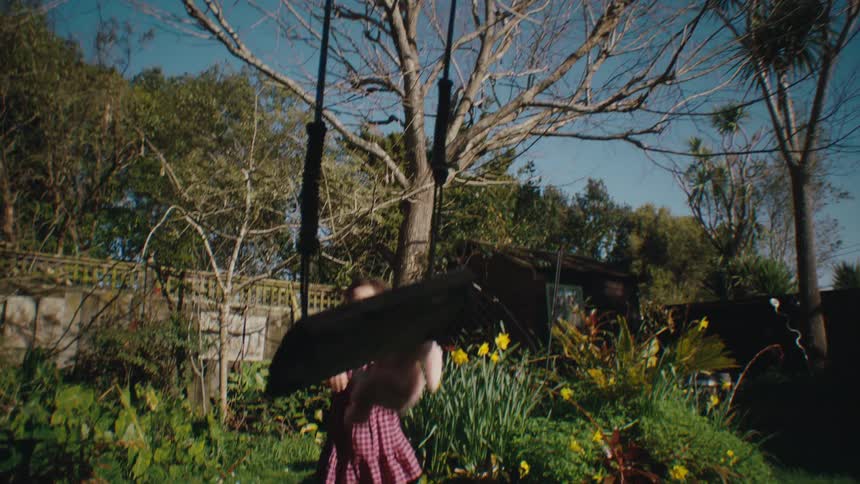 A young girl pushes a pink stuffed animal in a swing outdoors