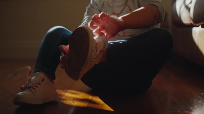 A child sits on the floor wearing jeans and a white shirt with colorful patterns adjusting her shoes