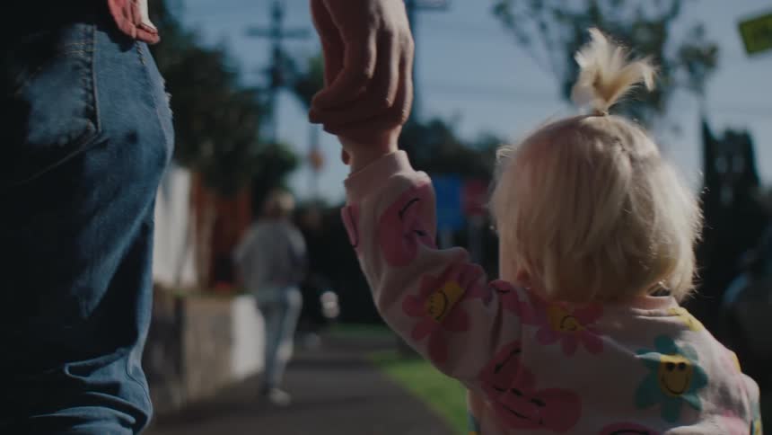 Little blonde girl walking on the sidewalk holding the hand of an adult person