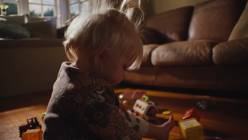 A blonde toddler joyfully playing with colorful toys in a cozy living room filled with natural light