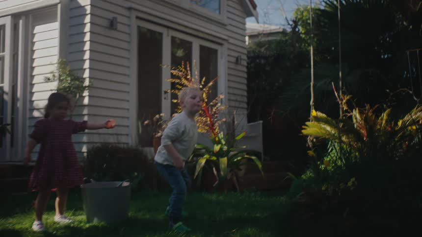 A couple of children play with water balloons in the backyard