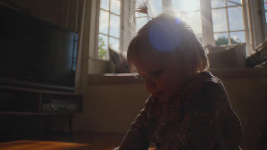 A child sitting on a wooden floor surrounded by various toys