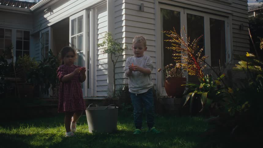Two children play with water balloons in the yard