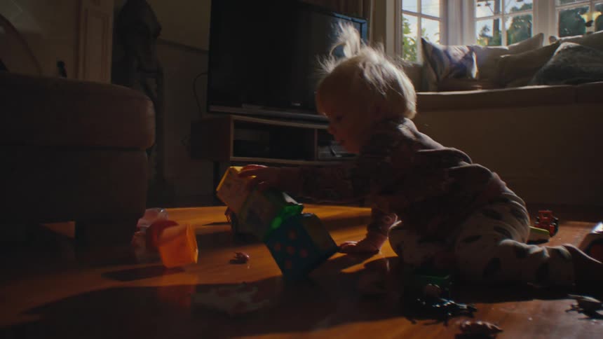 A young child plays with colorful stacking blocks on the living room floor welllit by natural light