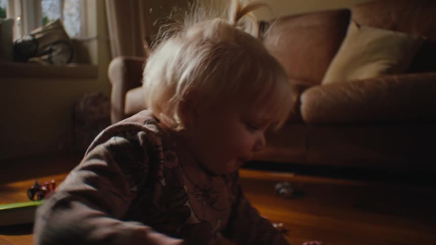 A female toddler plays with toys on a wooden living room floor