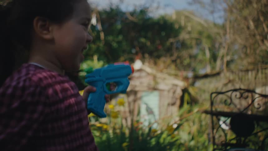 A girl runs in the backyard holding a blue and orange water gun