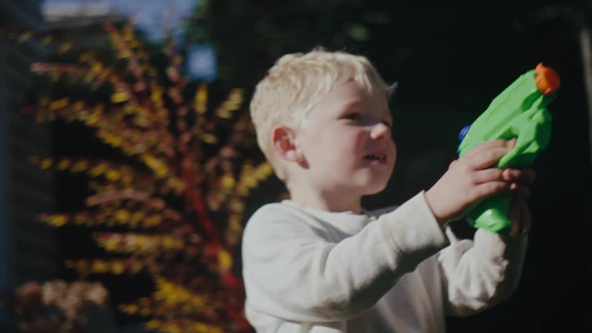 A boy is shooting a water gun outside