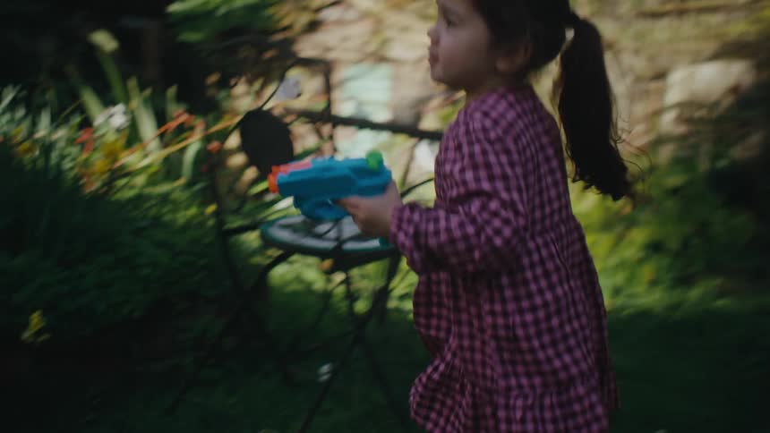 A girl runs in the backyard holding a blue and orange water gun
